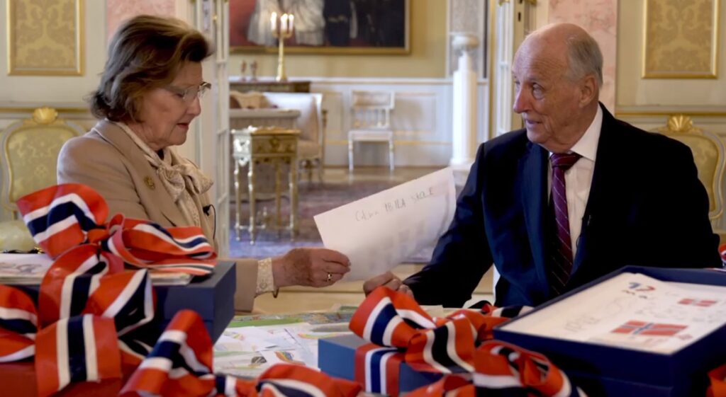 King Harald and Queen Sonja look at drawings sent to them by children to mark National Day 2021