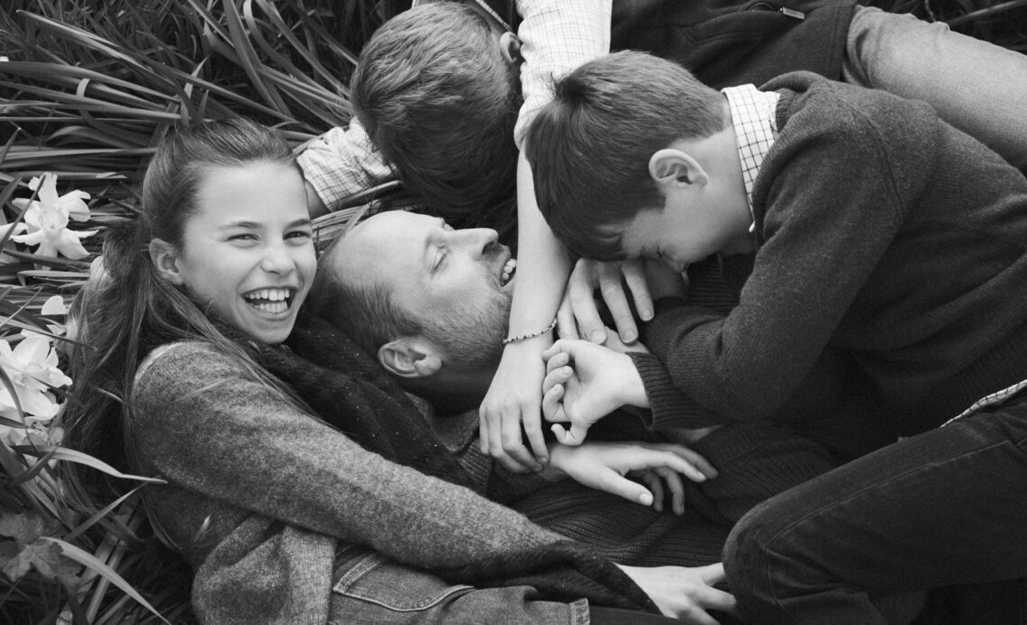 Prince William with George, Charlotte and Louis who are cuddling him.