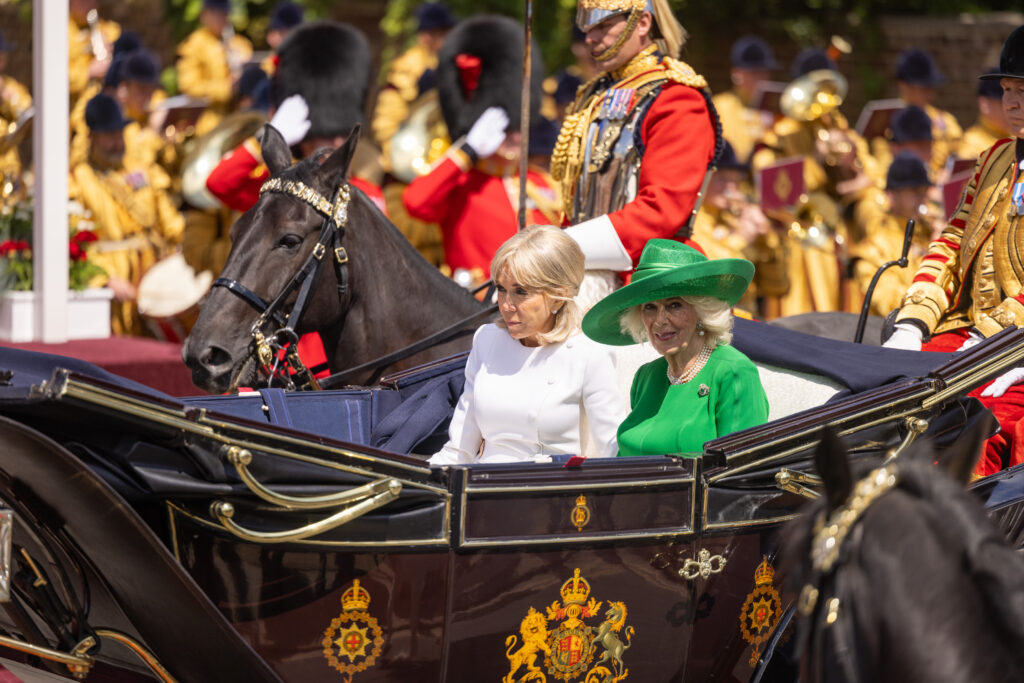 Queen Camilla rides in a semi state landau with Brigitte Macron at the start of the French State Visit to the UK. The Queen is wearing bright emerald green.