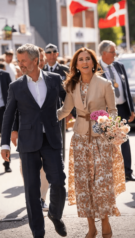 King Frederik and Queen Mary walk through a street in Grasten decked with Danish flags