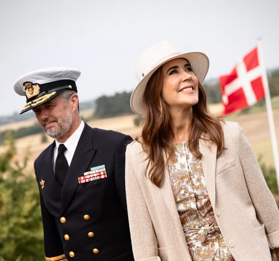 King Frederik and Queen Mary smile as they walk in front of a Danish flag