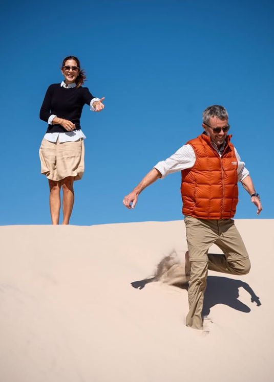 Queen Mary points to her husband, King Frederik, as he jumps down a dune during a day out in Saeby
