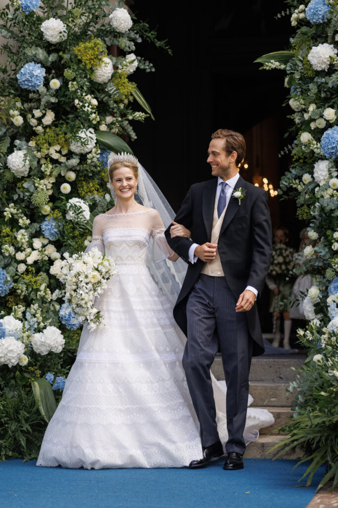 Princess Marie Caroline of Liechtenstein and Leopoldo Maduro Vollmer walk through an arch of blue and white flowers after their wedding in Vaduz
