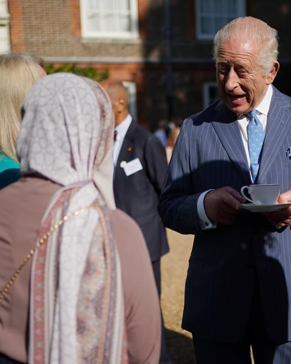 King Charles holds a cup and saucer as he talks to guests at a reception at Clarence House in London