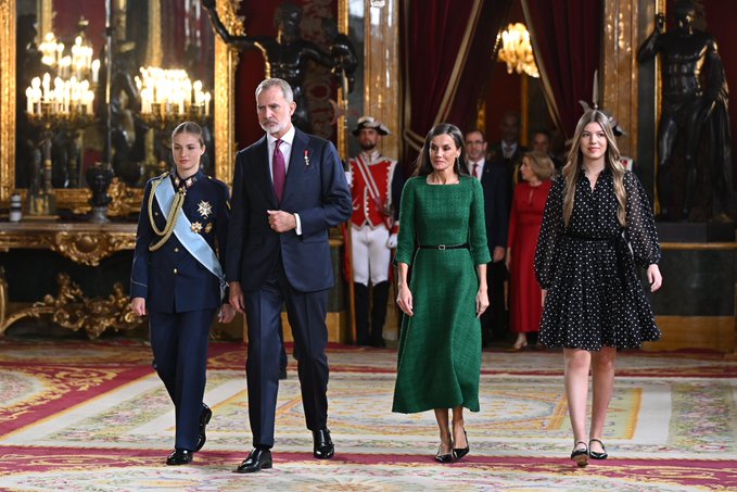 King Felipe and Queen Letizia walk across a room decked in tapestries