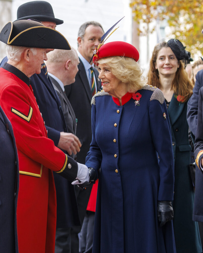 Queen Camilla shakes hands with a veteran who is wearing a red coat