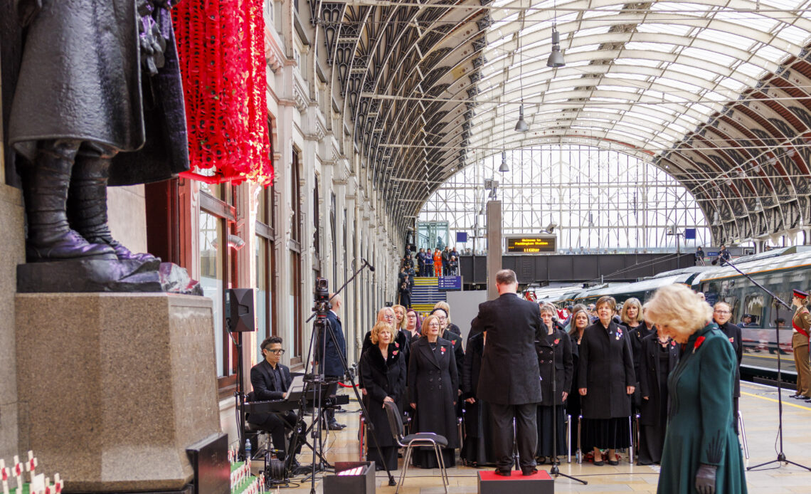 Queen Camilla bows her head in front of the memorial at Paddington Station which is surrounded with poppies