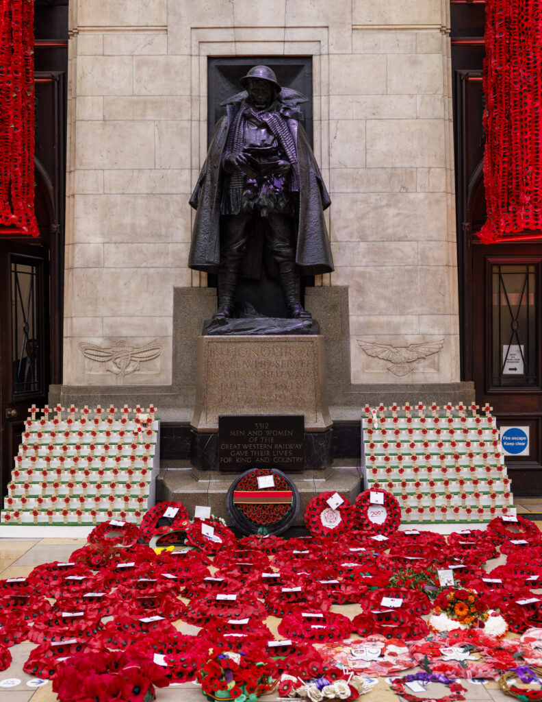 The magnificent bronze war memorial at Paddington station looks over a carpet of bright red poppy wreaths on Armistice Day 2025
