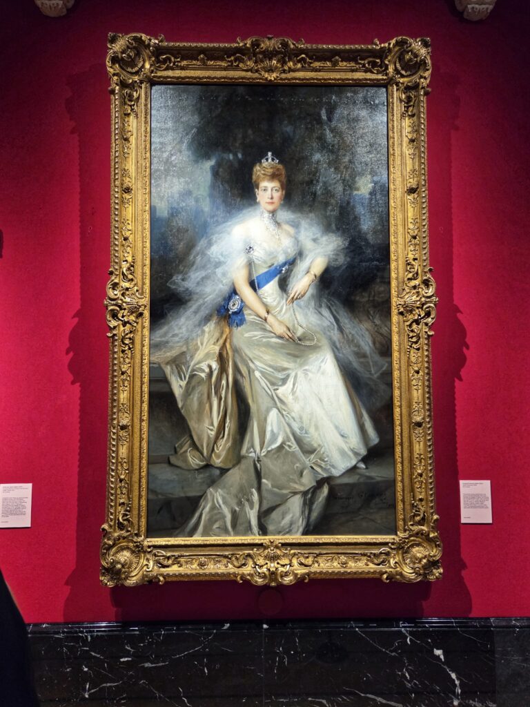 A portrait of Queen Alexandra sits on a bright red wall