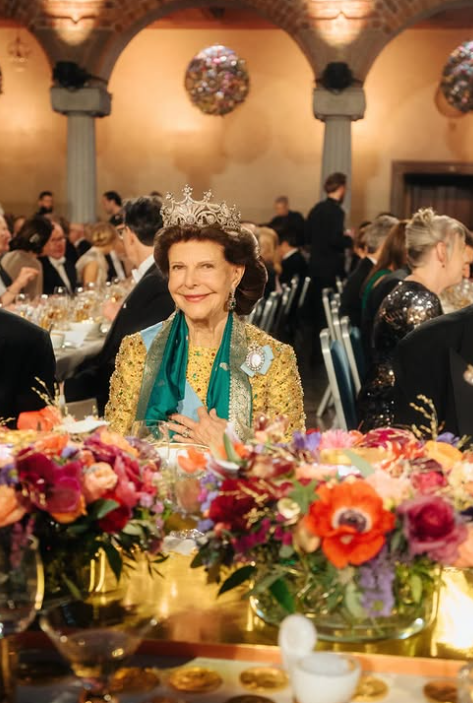 Queen Silvia of Sweden wears a yellow ball gown with a bright green scarf
