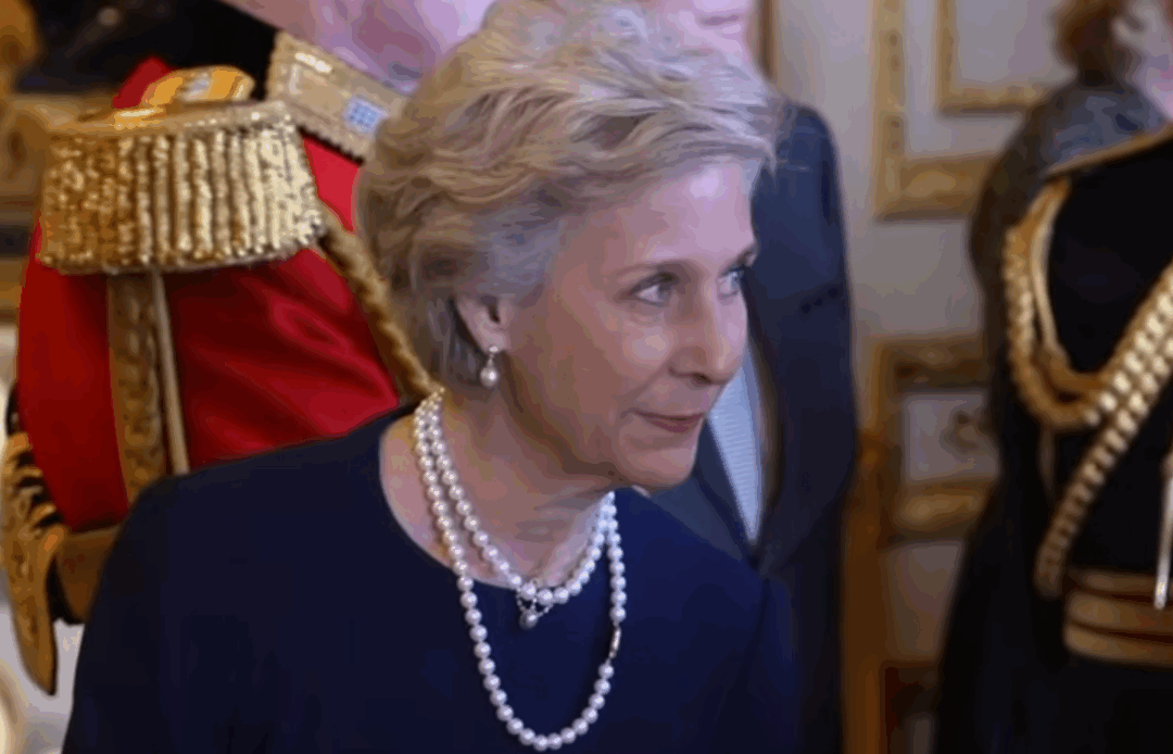 The Duchess of Gloucester wears a dark dress and a pearl necklace