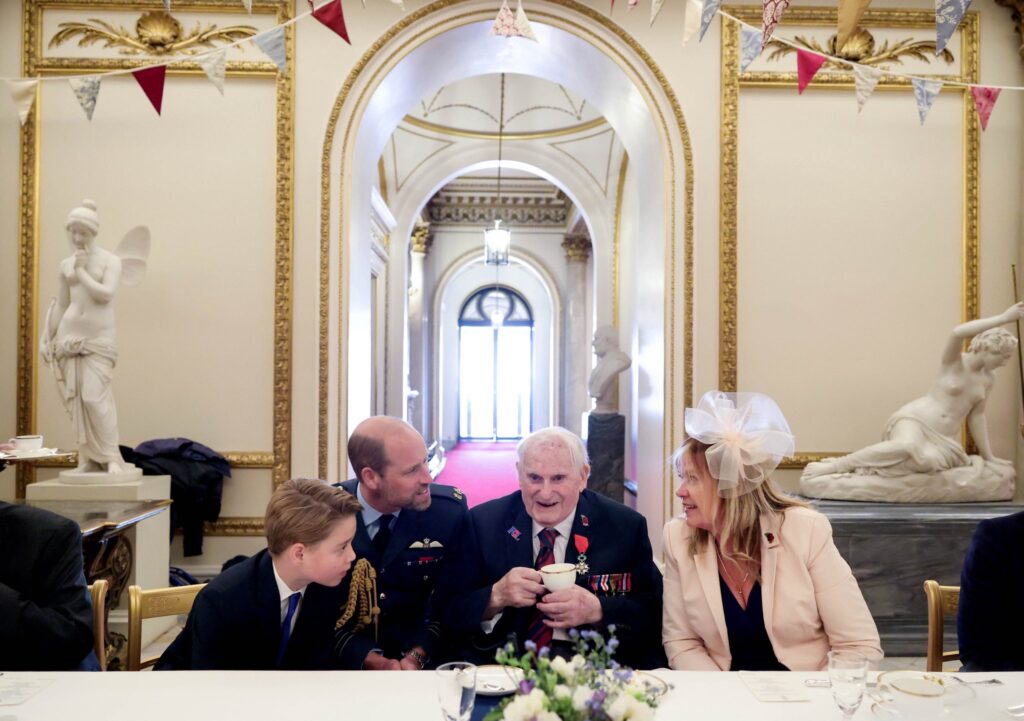 Prince George leans in to talk to a veteran while Prince William talks to a relative