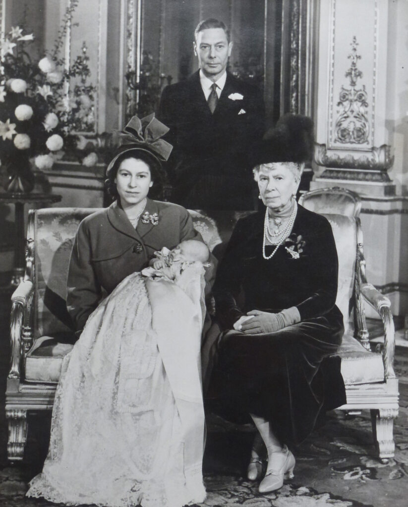 Queen Elizabeth II holds King Charles III with Queen Mary at her side and King George VI standing behind them