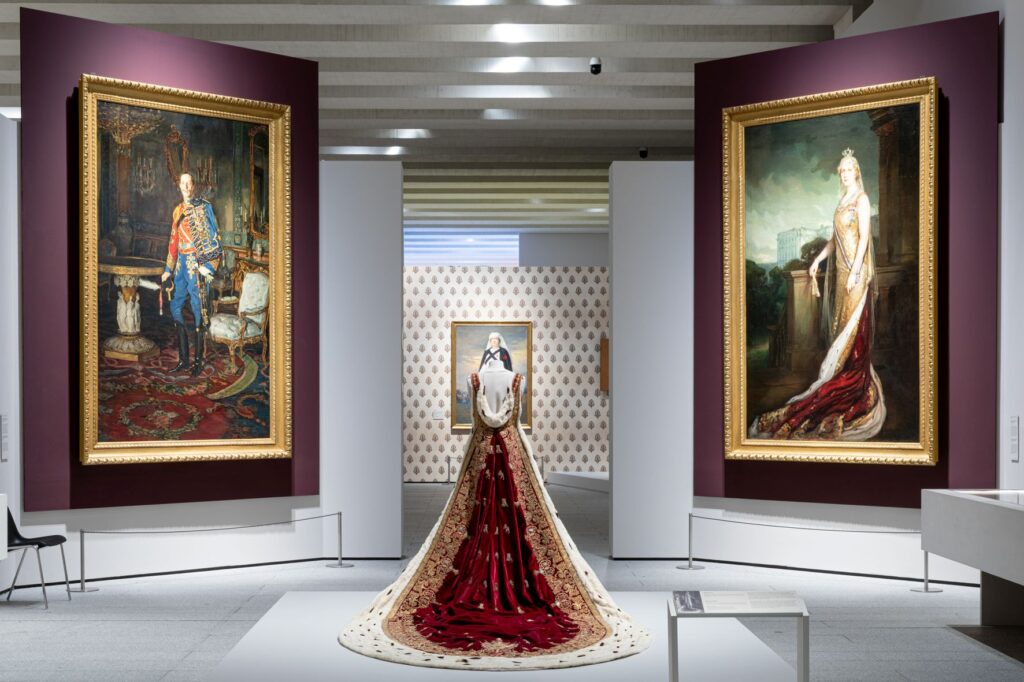 An ermine trimmed robe stands between two portraits in an exhibition 