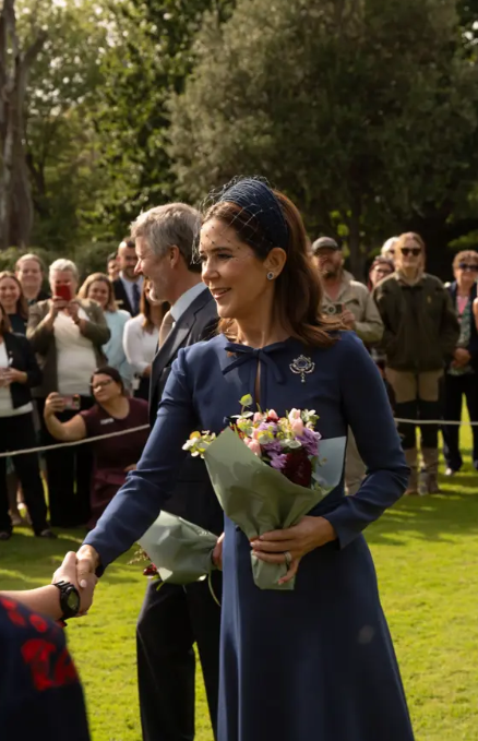 Queen Mary wears navy and shakes hands in a garden