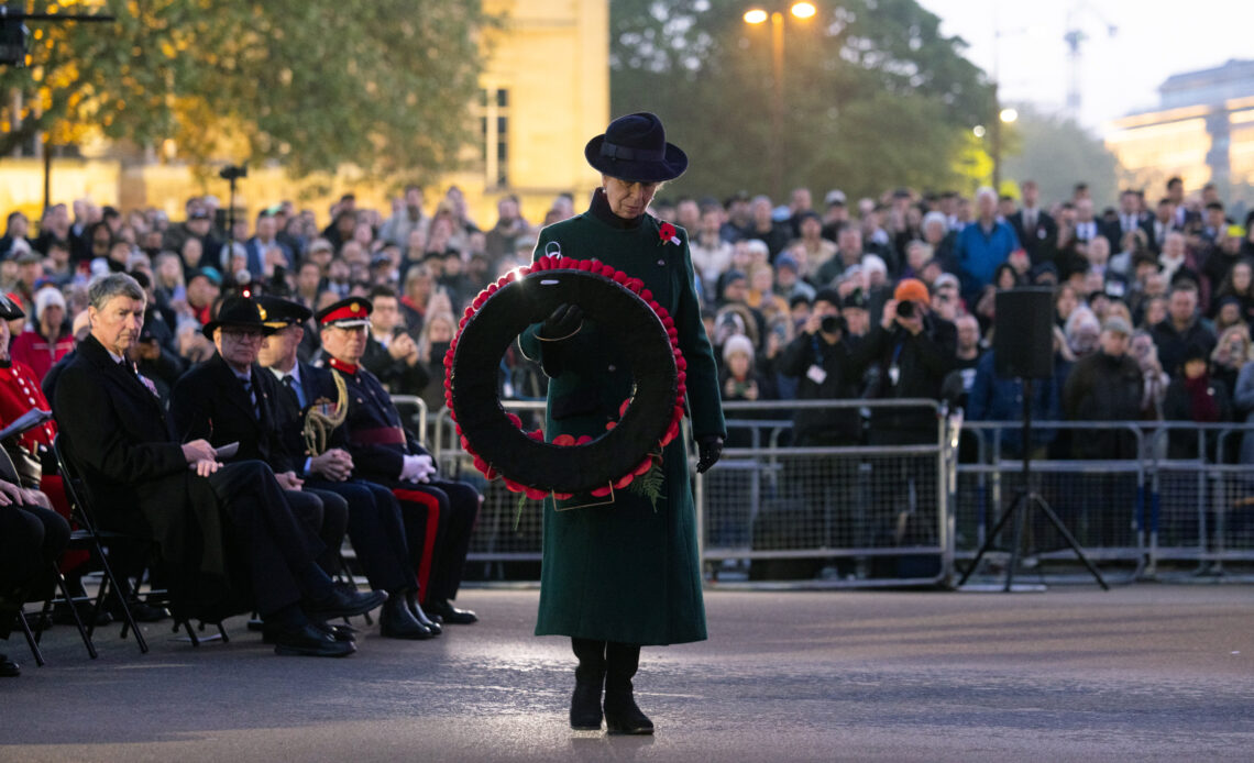 Princess Anne wears a green coat and carries a wreath of poppies