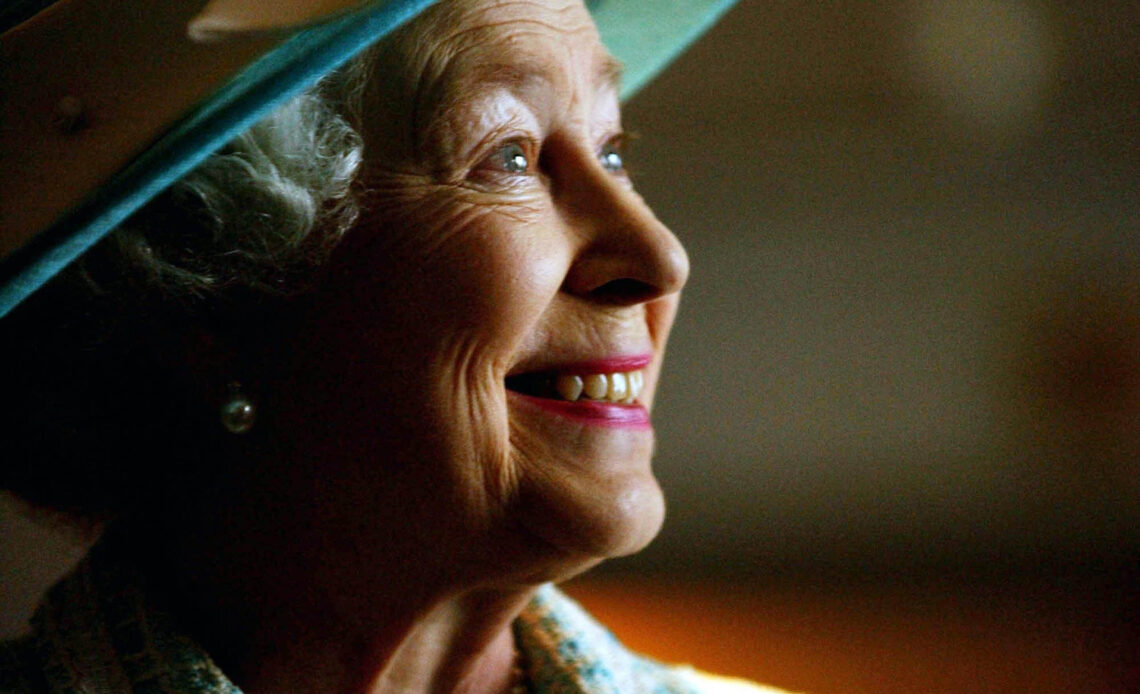 Queen Elizabeth II in a wide brimmed hat turns to one side and smiles