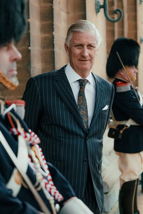 A man in a pin stripe suit stands between two soldiers in dress uniform