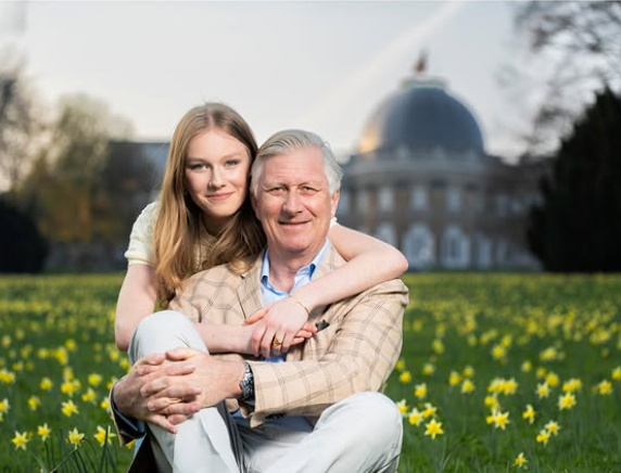 A man sits in the grass with his daughter putting her arms around his shoulders