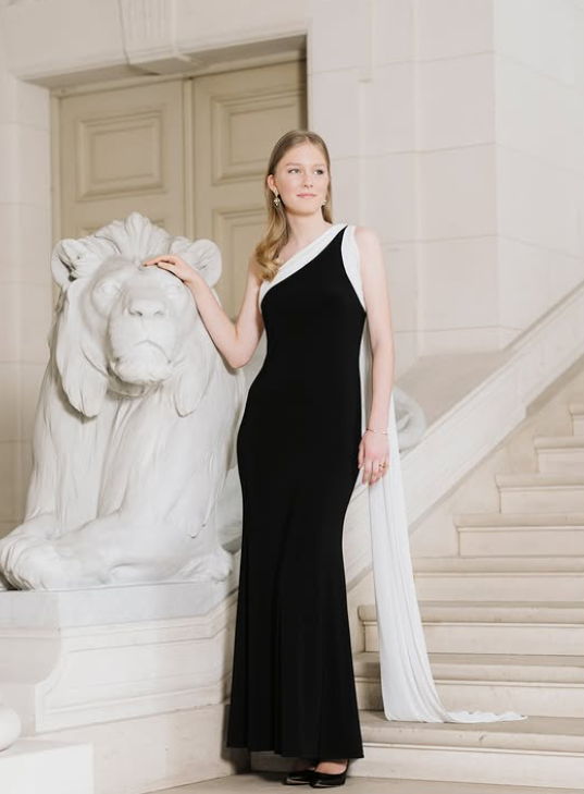 A young woman in a black and white evening gown stands on a marble staircase