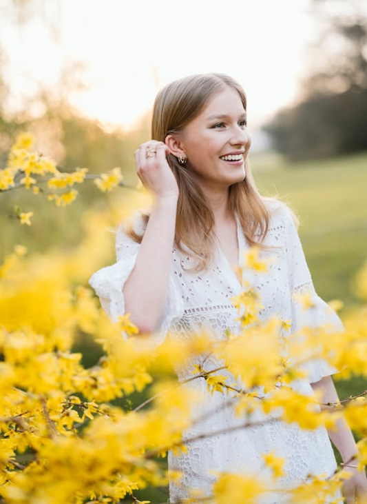 A young woman in a white dress stands in a field of yellow flowers