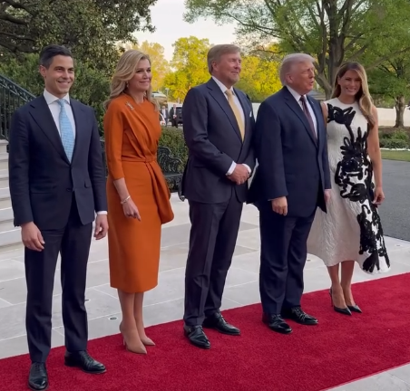 Queen Maxima in an orange dress stands with King Willem-Alexander and Donald and Melania Trump on a red carpet