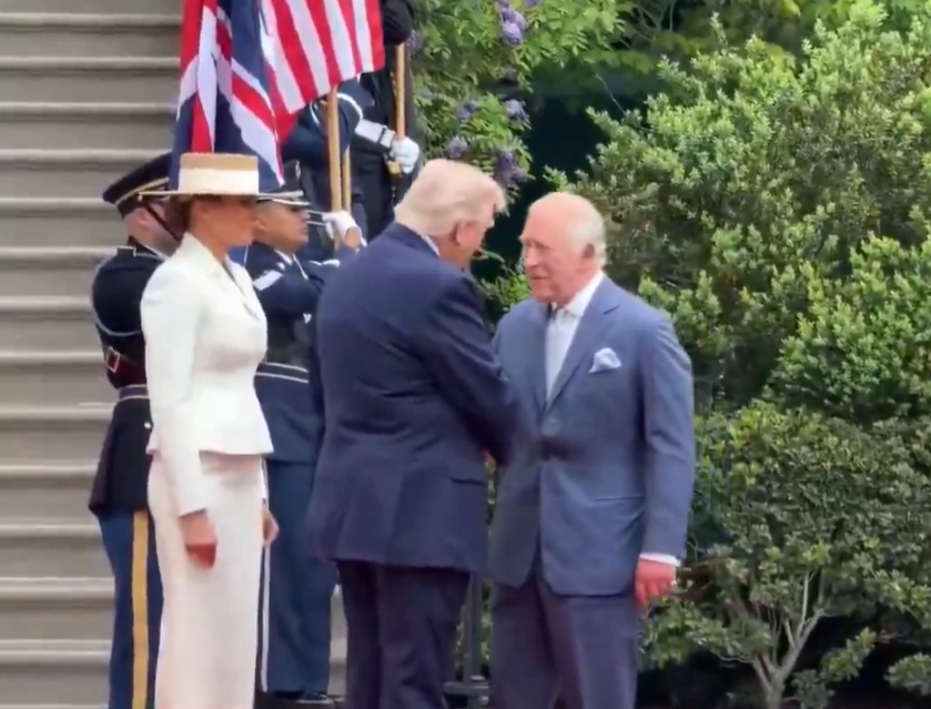 King Charles shakes hands with Donald Trump while Melania Trump watches - she is wearing a wide brimmed straw hat with cream coloured band