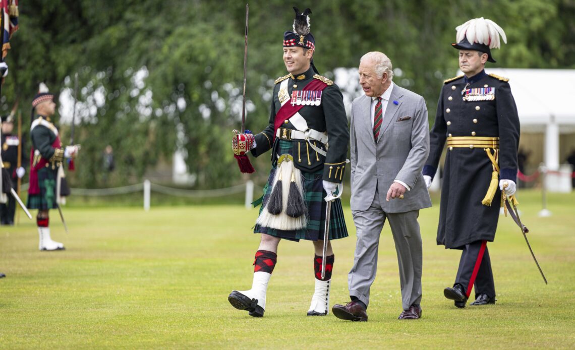 King Charles wears a gre suit and walks across a lawn
