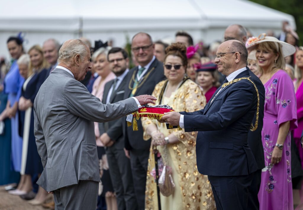 King Charles, in a grey suit, lays his hands on a red velvet cushion carrying the keys of the City of Edinburgh