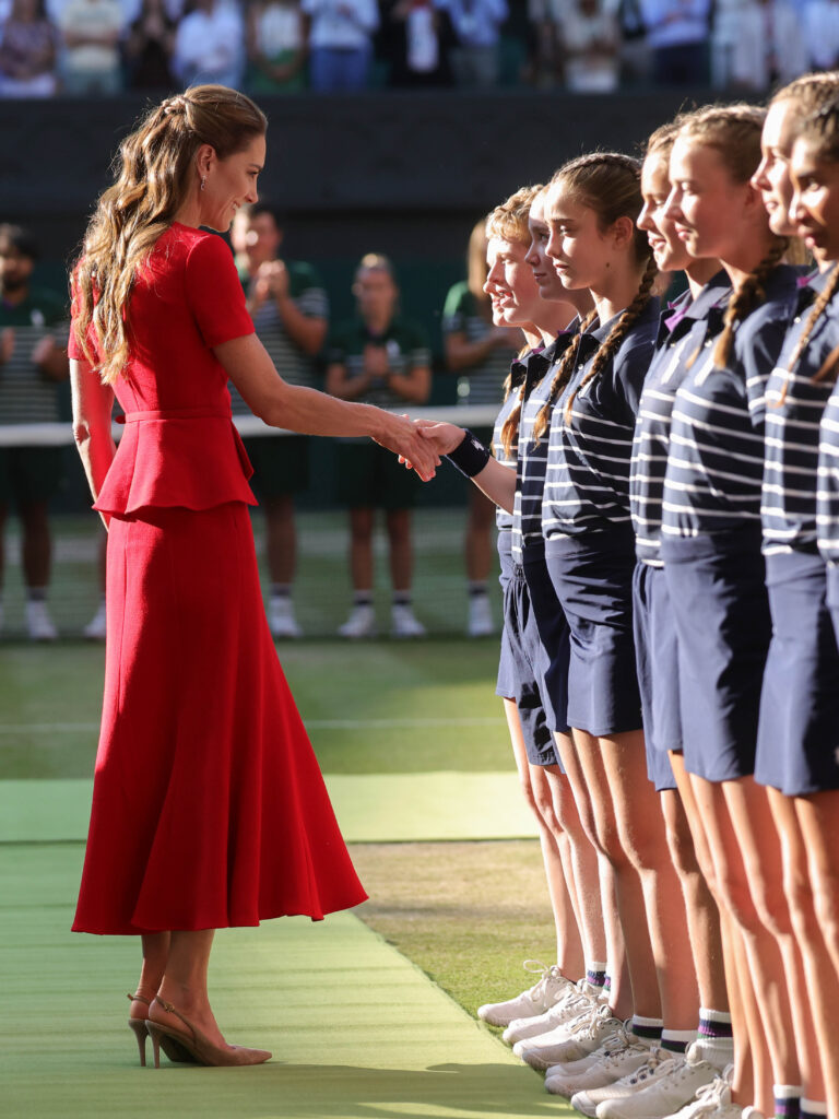 The Princess of Wales, inn a red dress, shakes hands with ballboys at Wimbledon