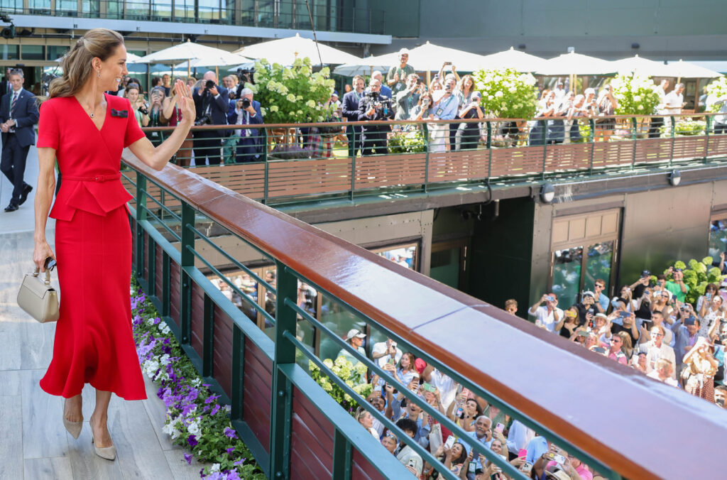The Princess of Wales, in a red dress, waves to the crowd at Wimbledon as she walks across a bridge